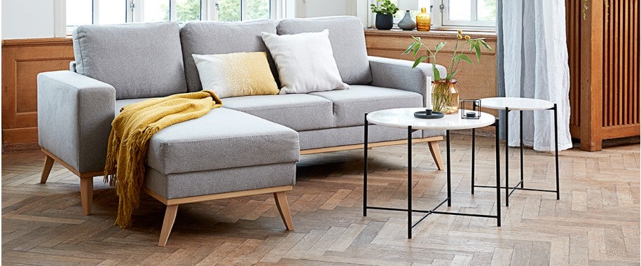 A Scandinavian-inspired living room with a minimalistic style that emphasizes clean lines, modern décor, and natural touches. The centerpiece is the ARENDAL grey sofa with chaise, complemented by the SOCHA yellow throw blanket.